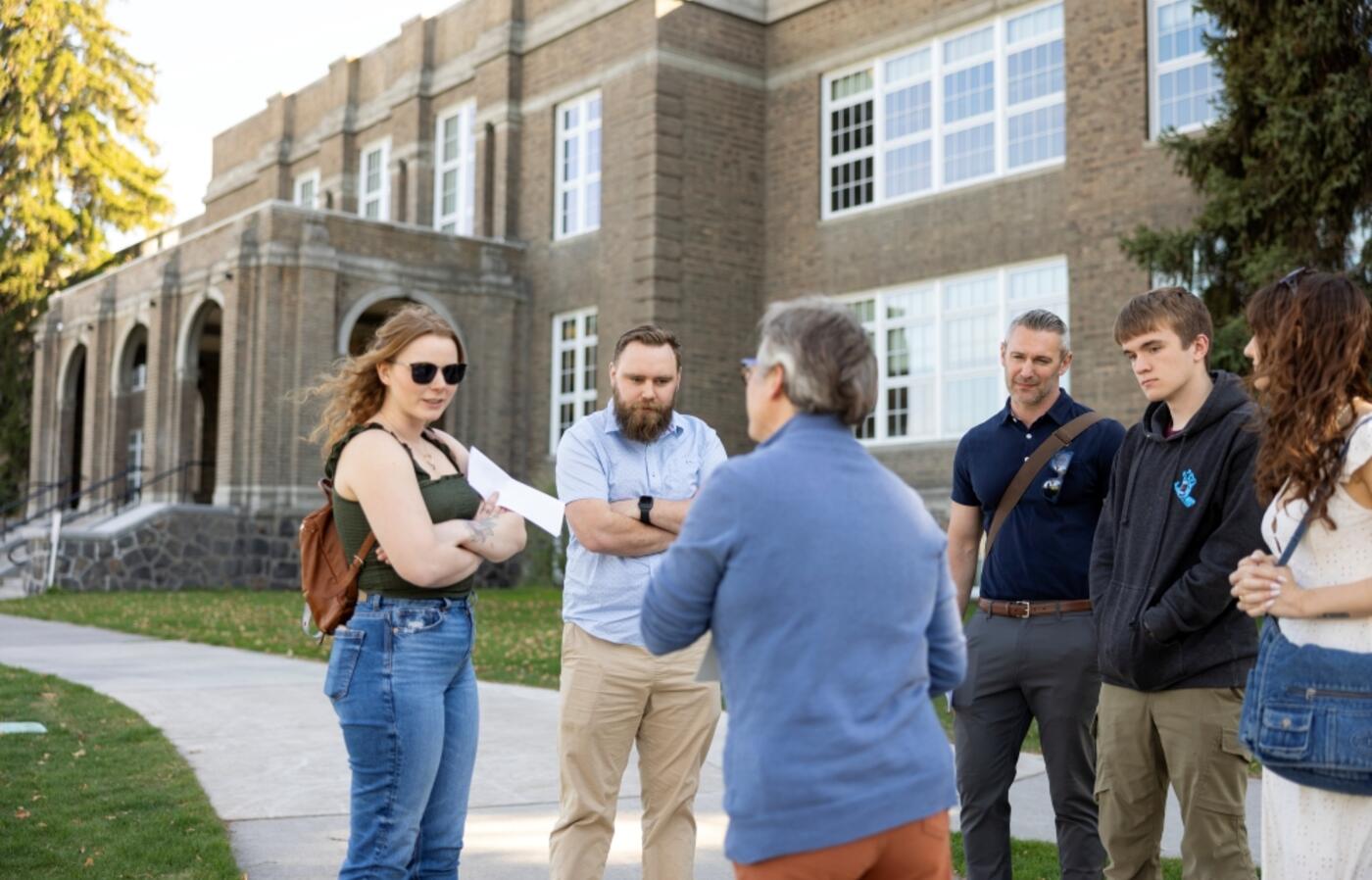 Students and faculty standing outside, in front of a building, listening to tour guide