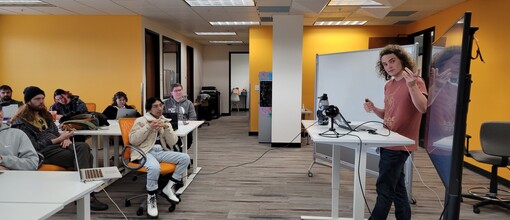 Professor speaking in front of student, pointing to a smartboard