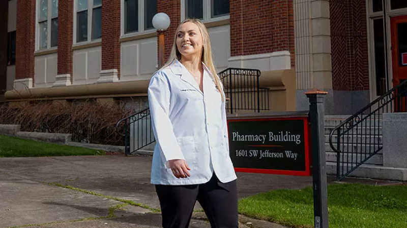 student in front of pharmacy school sign