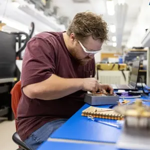 Mechanical Engineering Student siting at a desk working with tools on a metal box