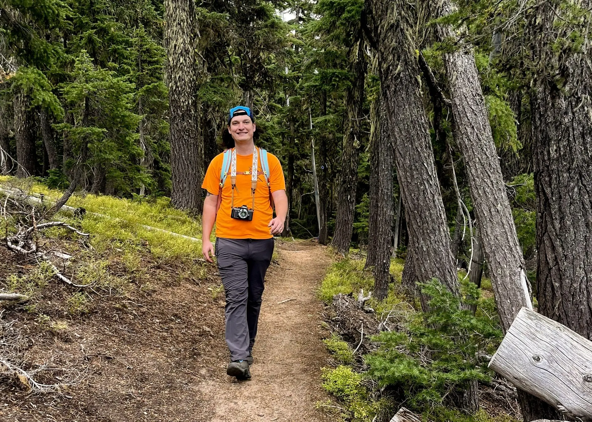 A man in an orange shirt walks down a trail in the forest. 