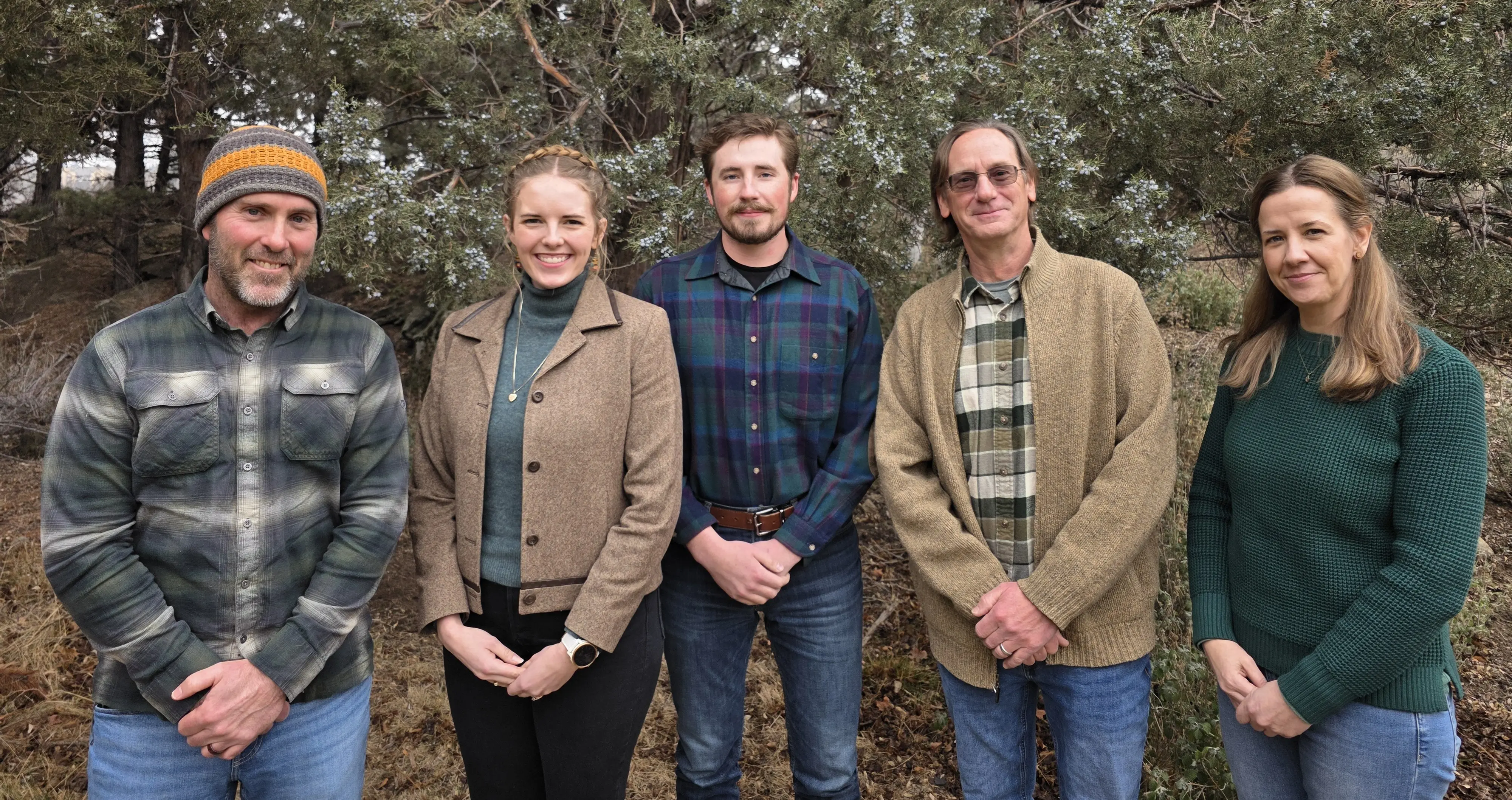 A group of people in green and khaki clothes stand with hands clasped
