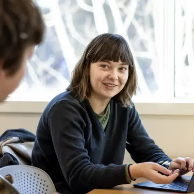 Woman looking to the side at a deskmate, both are sitting at a table with a laptop