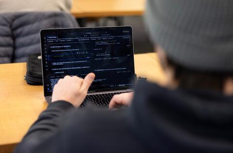 Person sitting in front of laptop with github up on the screen, from the POV of behind the person