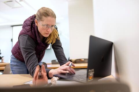 Woman standing while leaning over laptop with a pencil in her hand