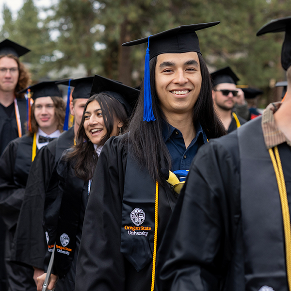 graduates in caps and gowns, one smiling at the camera.
